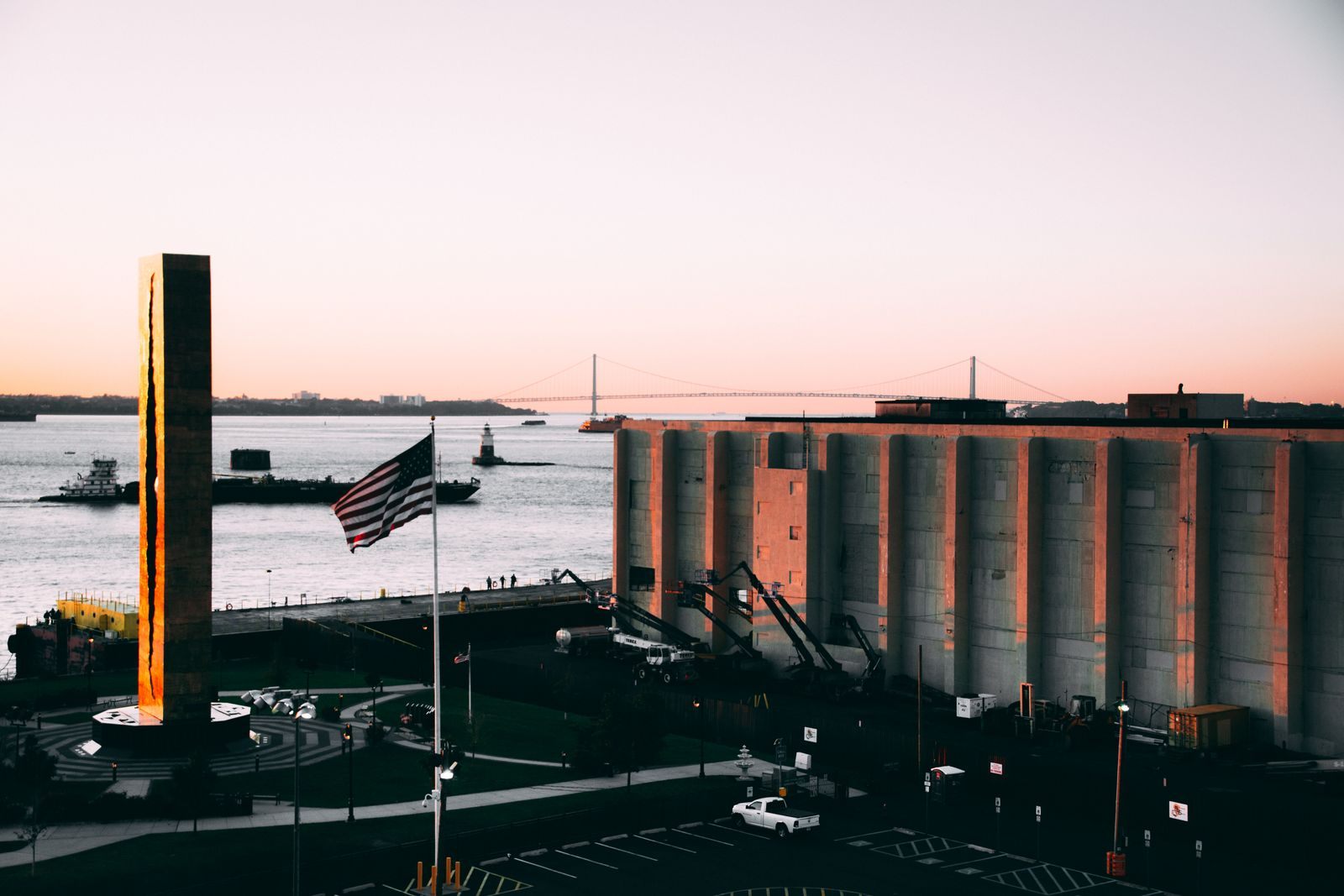 American flag on a waterfront pier at sunset with a bridge and harbor behind, like the home ports of US based cruise lines