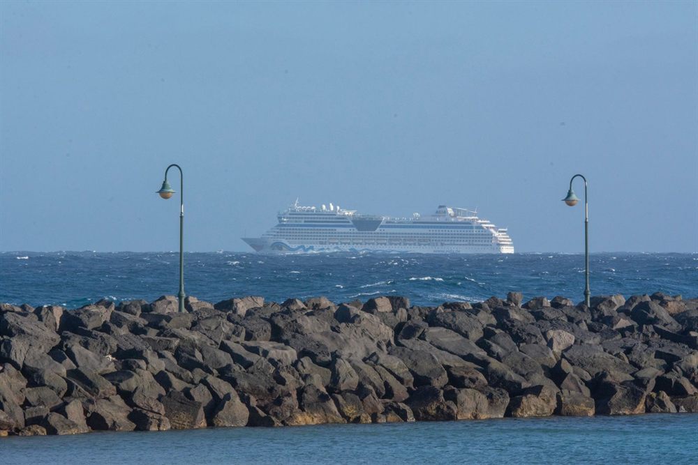Cruise ship on the horizon beyond a rock breakwater and harbor lamp posts