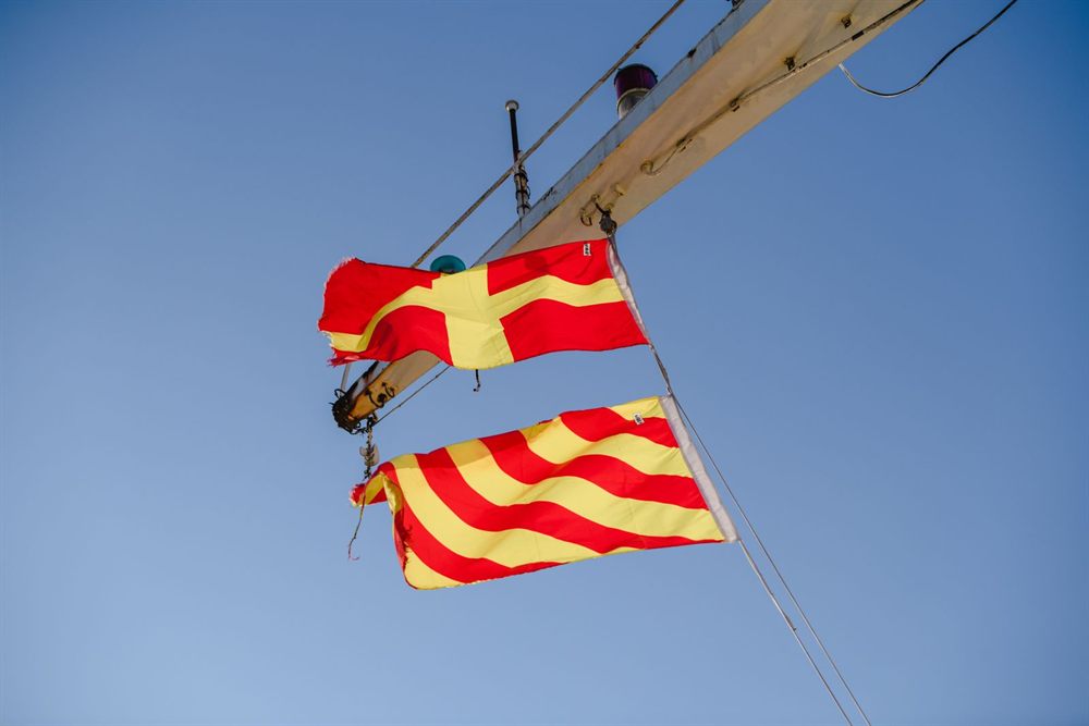 Red and yellow nautical signal flags flying from a mast against a blue sky