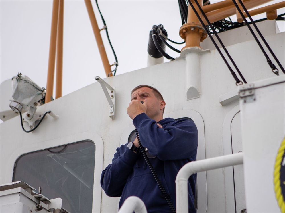 Ship’s officer in a navy jacket speaking into a radio handset on deck